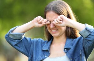 A woman outside rubbing her eyes as she suffers from itchy, dry eyes