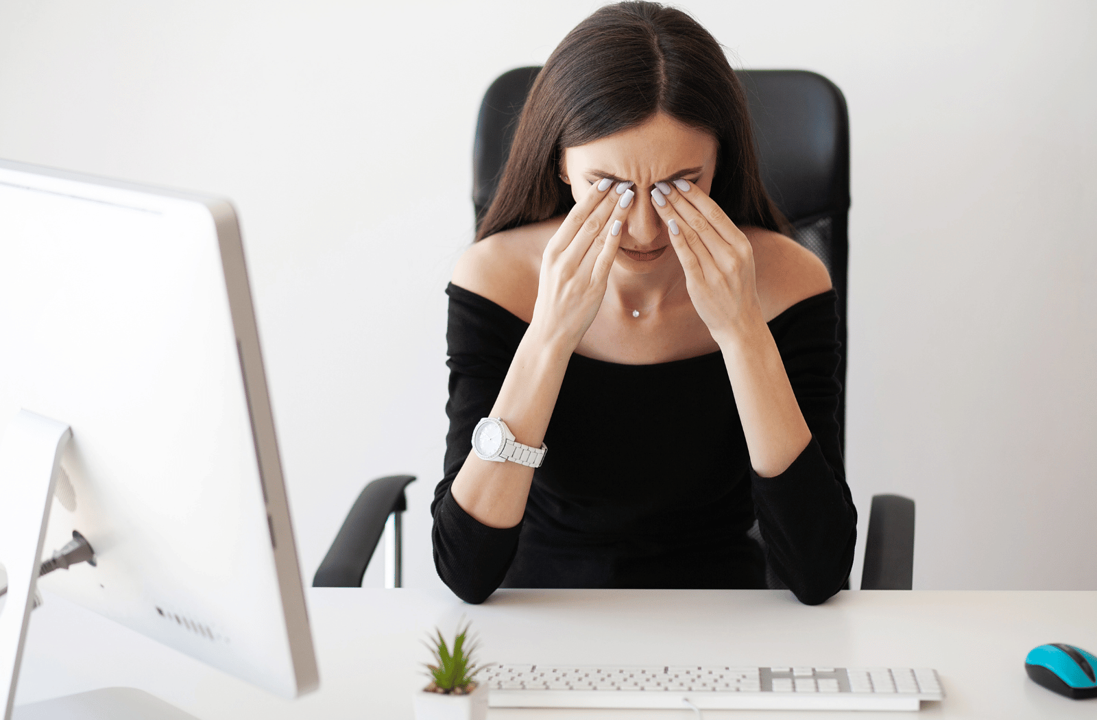 A woman rubbing her strained and dry eyes while sitting at her desk