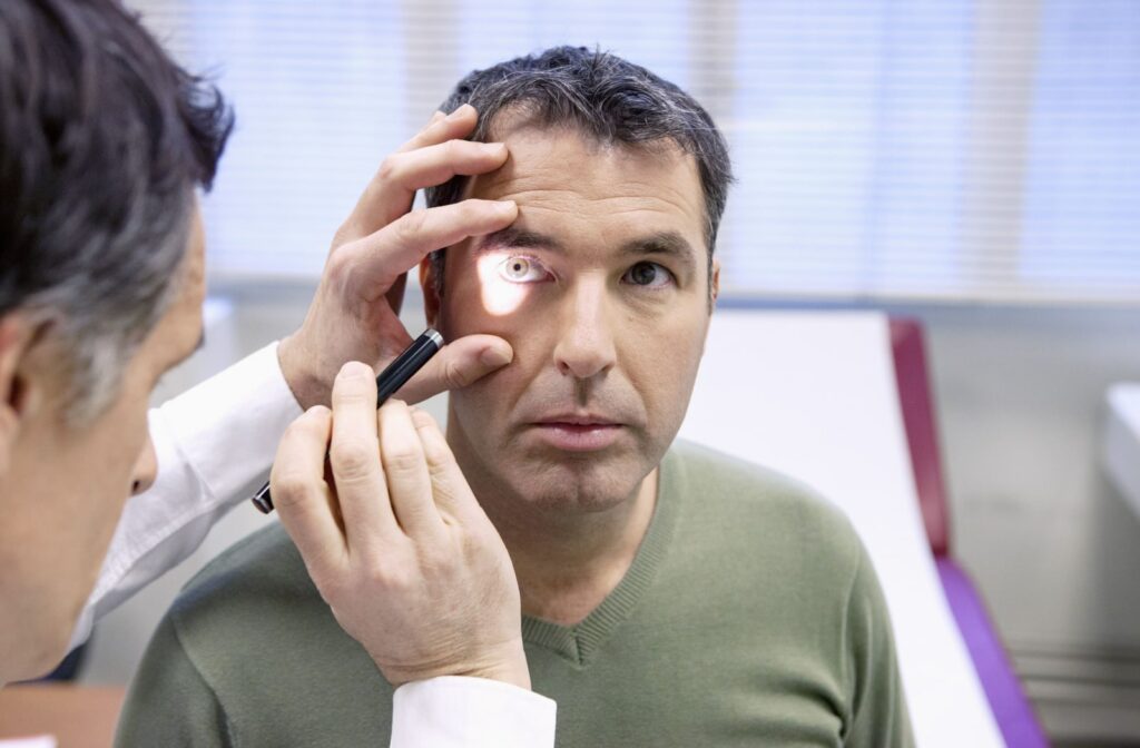 Close-up of a man having his eyes examined while an optometrist shines a small light into his right eye and gently holds it open