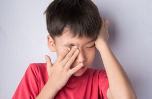 A young boy in a red shirt rubbing his eyes