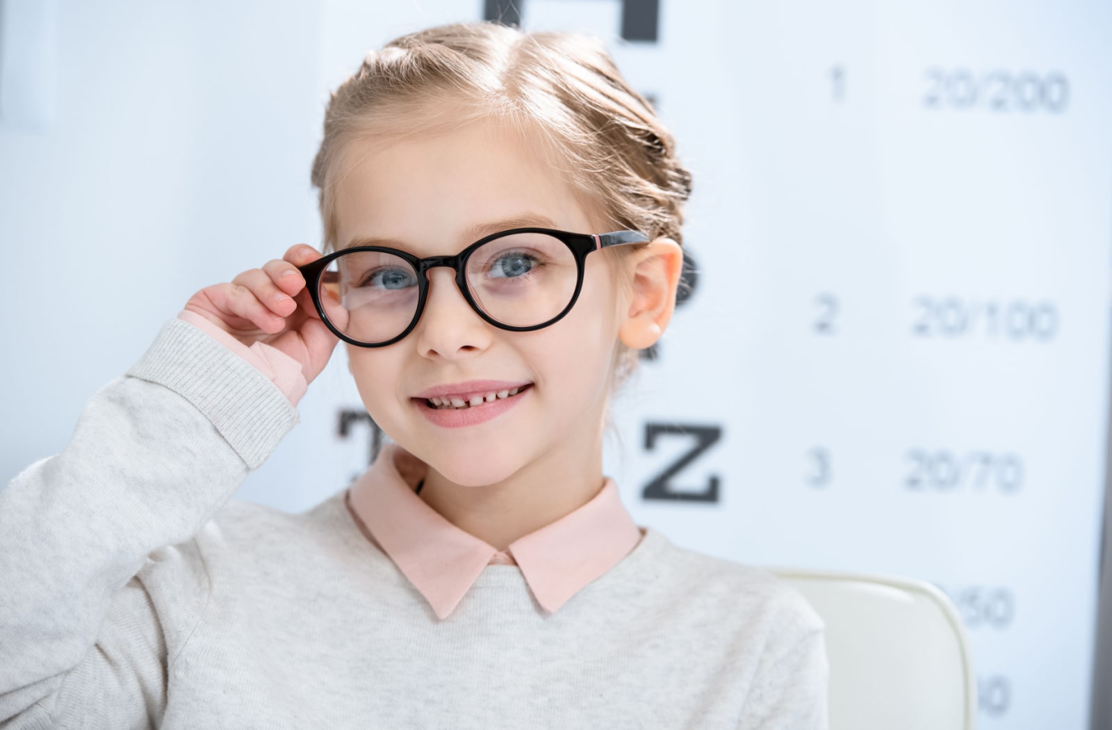 A young girl trying on glasses at the optometrist's office, and she is standing in front of a Snellen eye chart.