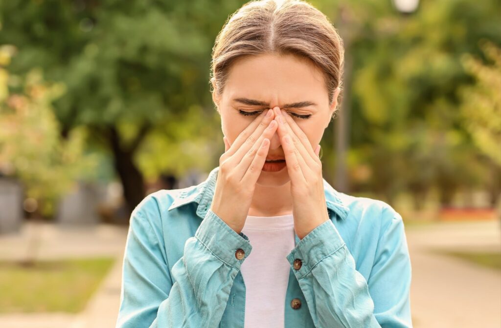 A woman experiencing allergies rubbing her eyes with both hands.