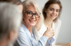 Older adult businesswoman smiling wearing glasses in a meeting.