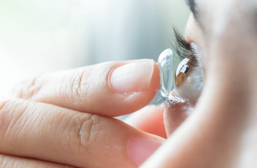 Close up of a woman holding a scleral lens on one finger, gently placing it on her brown eye