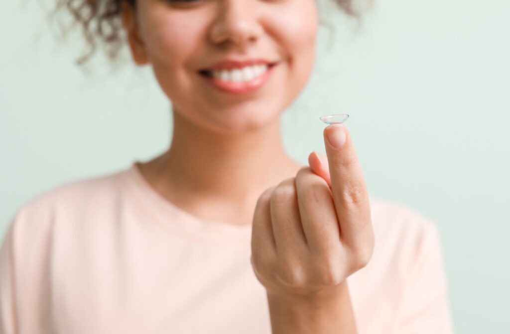 Smiling woman holding a contact lens on her fingertip.