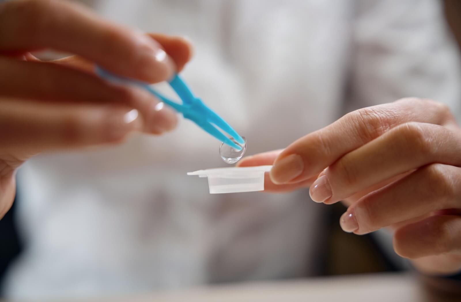 Person using tweezers to remove a contact lens from a storage case.