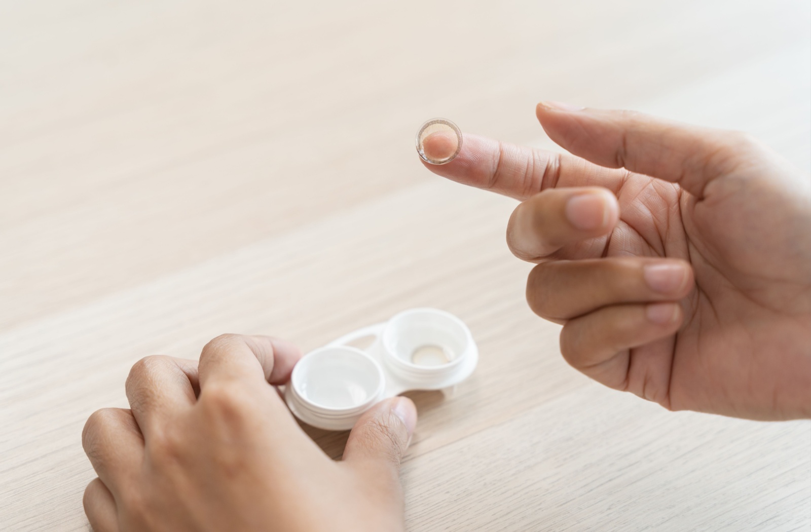 A close-up image of a person taking a scleral contact lens out of a white case.