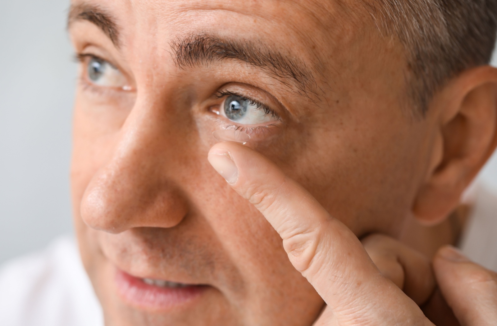 A middle-aged adult putting their bifocal contact lens in their eye.