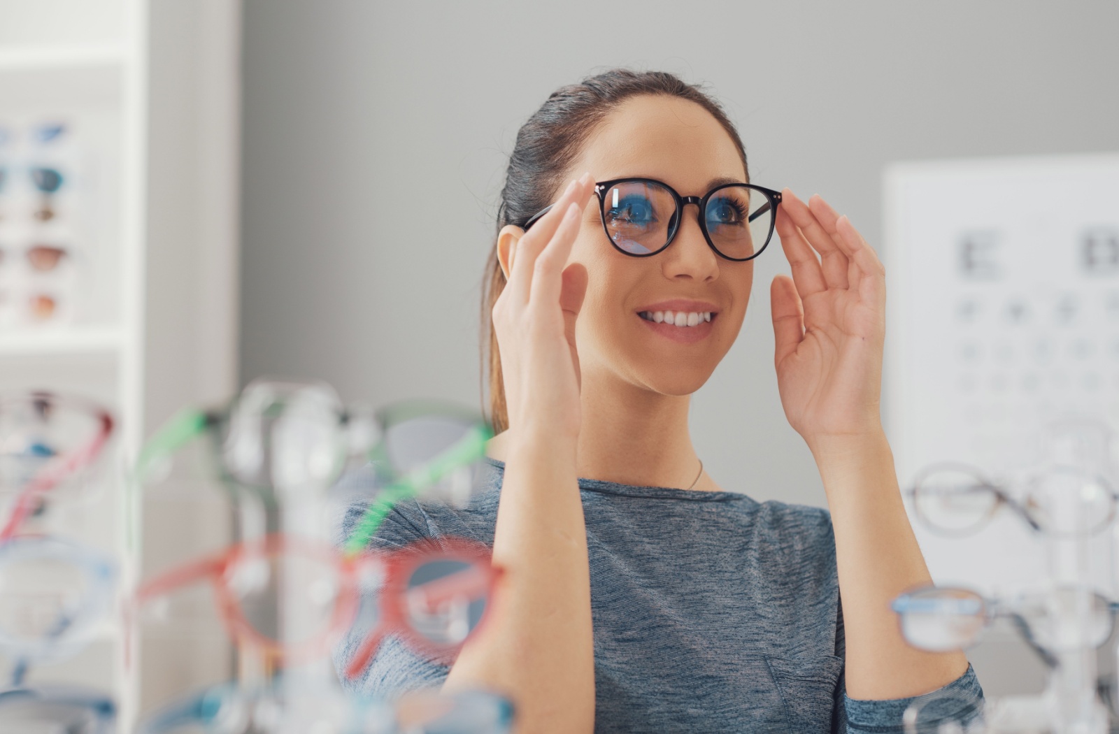 A smiling adult tries on new glasses frames in their eye doctor's showroom.