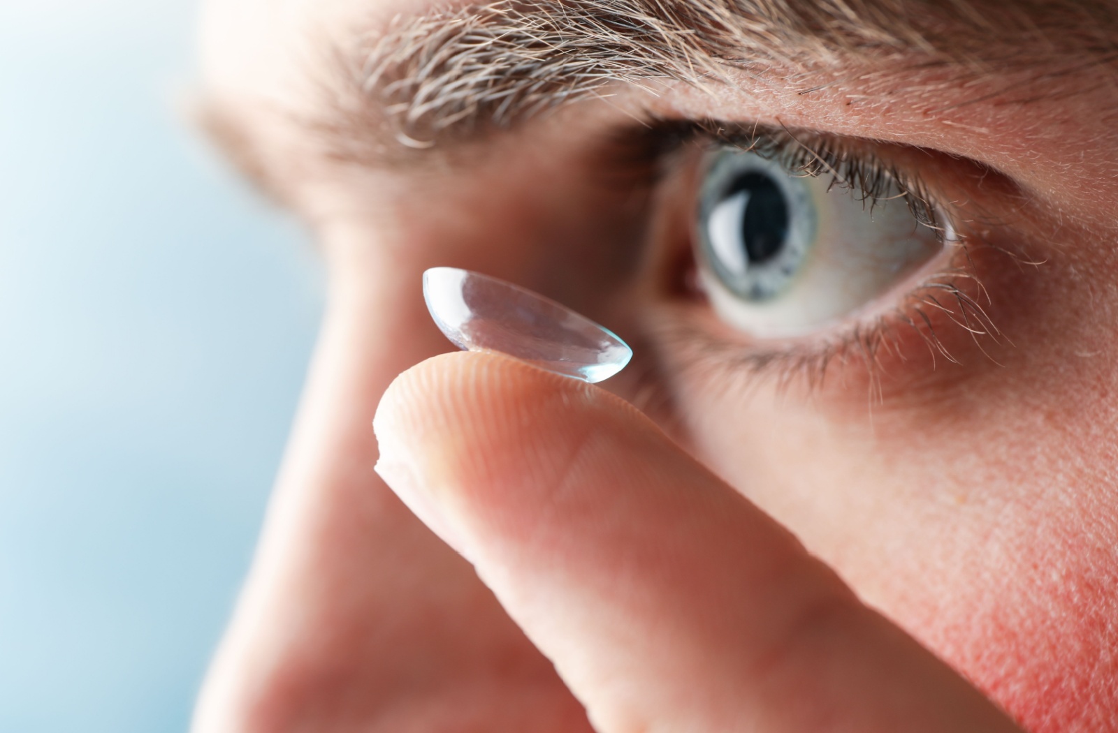 A close-up of someone inserting a contact lens into their eye.