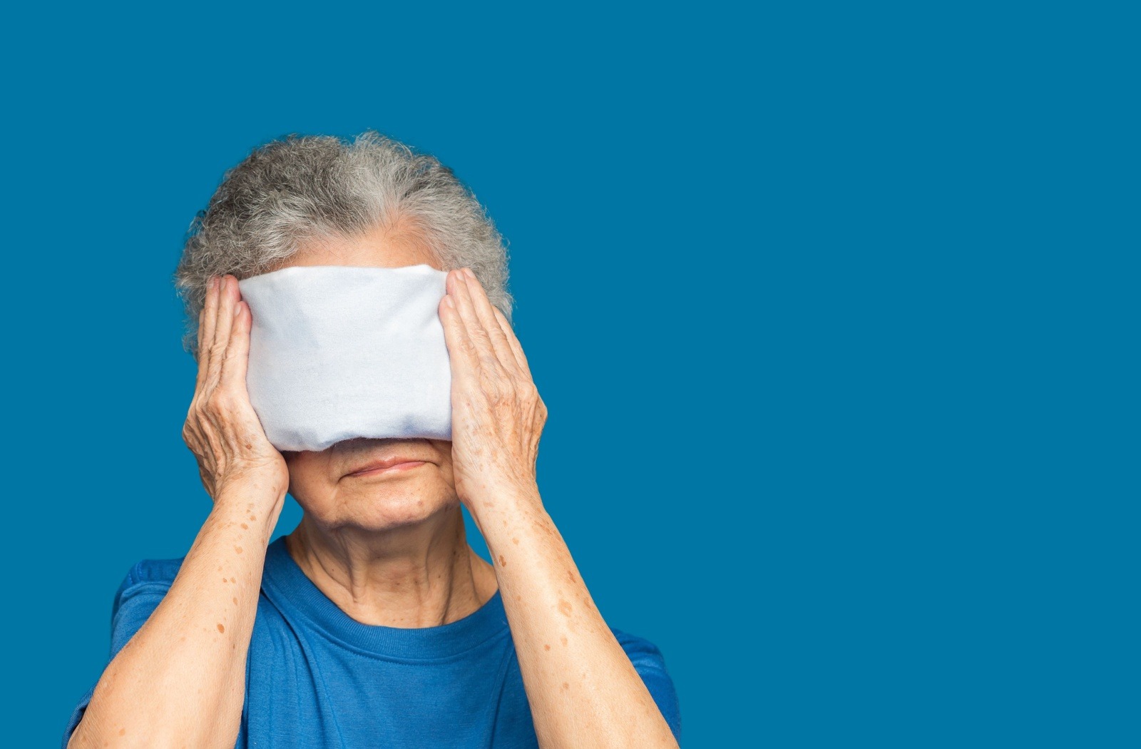 Older adult with a warm compress on their eyes to unclog their meibomian glands